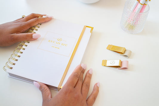 Person holding a spiral-bound notebook with decorative clips on a light surface