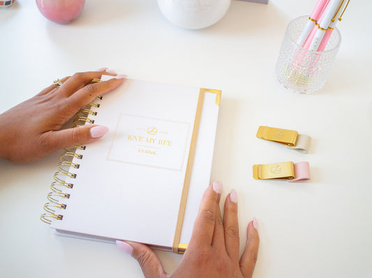 Person holding a spiral-bound notebook with decorative clips on a white surface