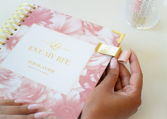 Planner with pink floral design and gold accents, held by a hand.