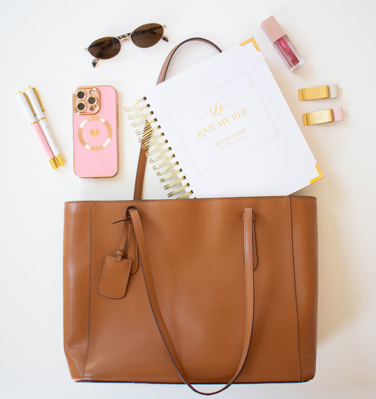Brown tote bag with phone, sunglasses, and stationery items on a white background