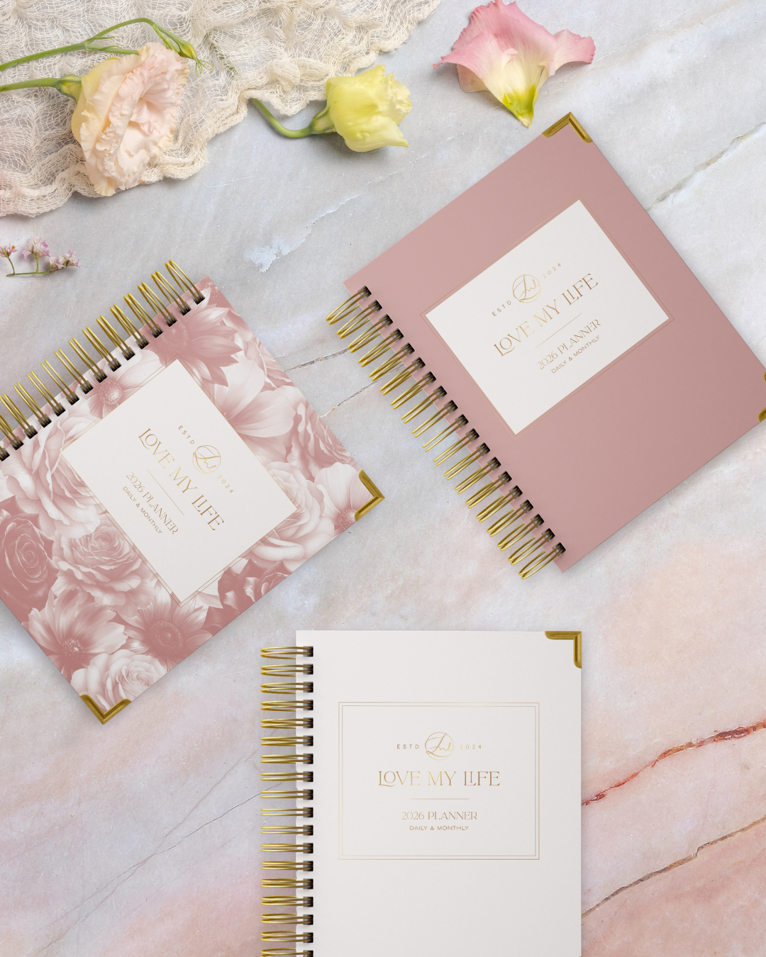Three spiral-bound planners with floral designs on a marble surface.