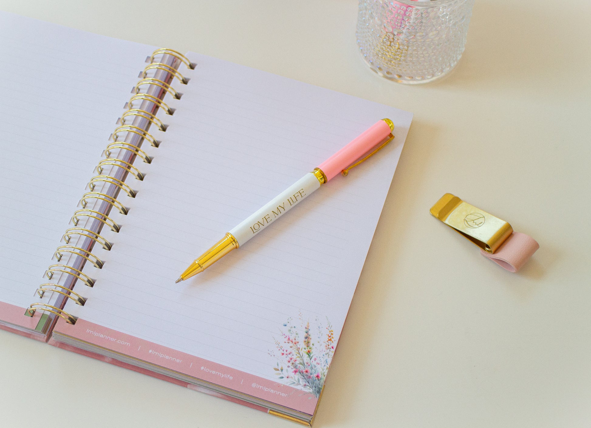 Pink pen and watch on a notebook with a decorative glass item in the background