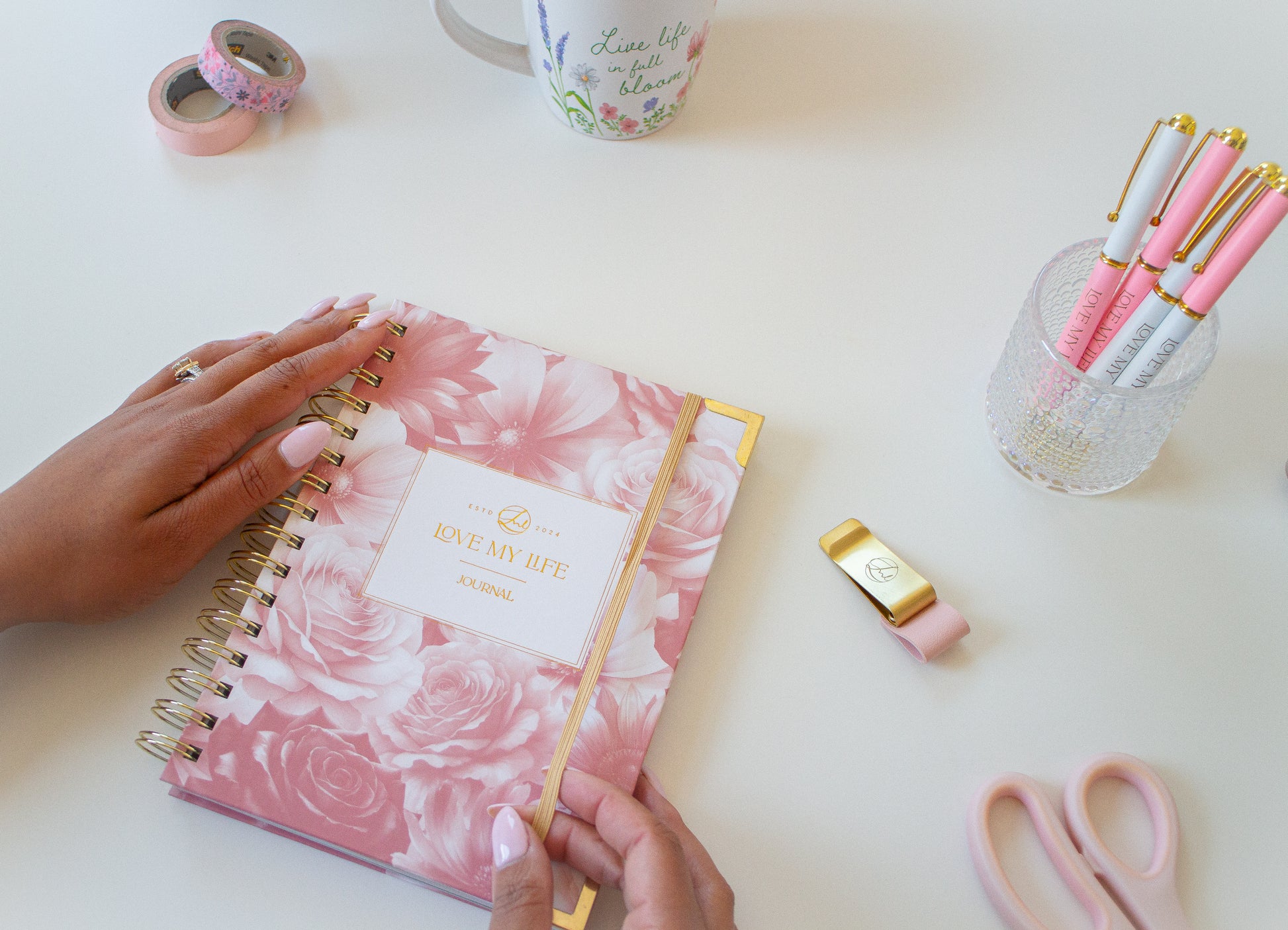 Pink floral notebook on a white surface with stationery items