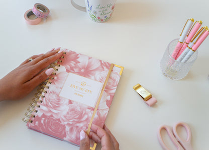 Pink floral notebook on a white surface with stationery items