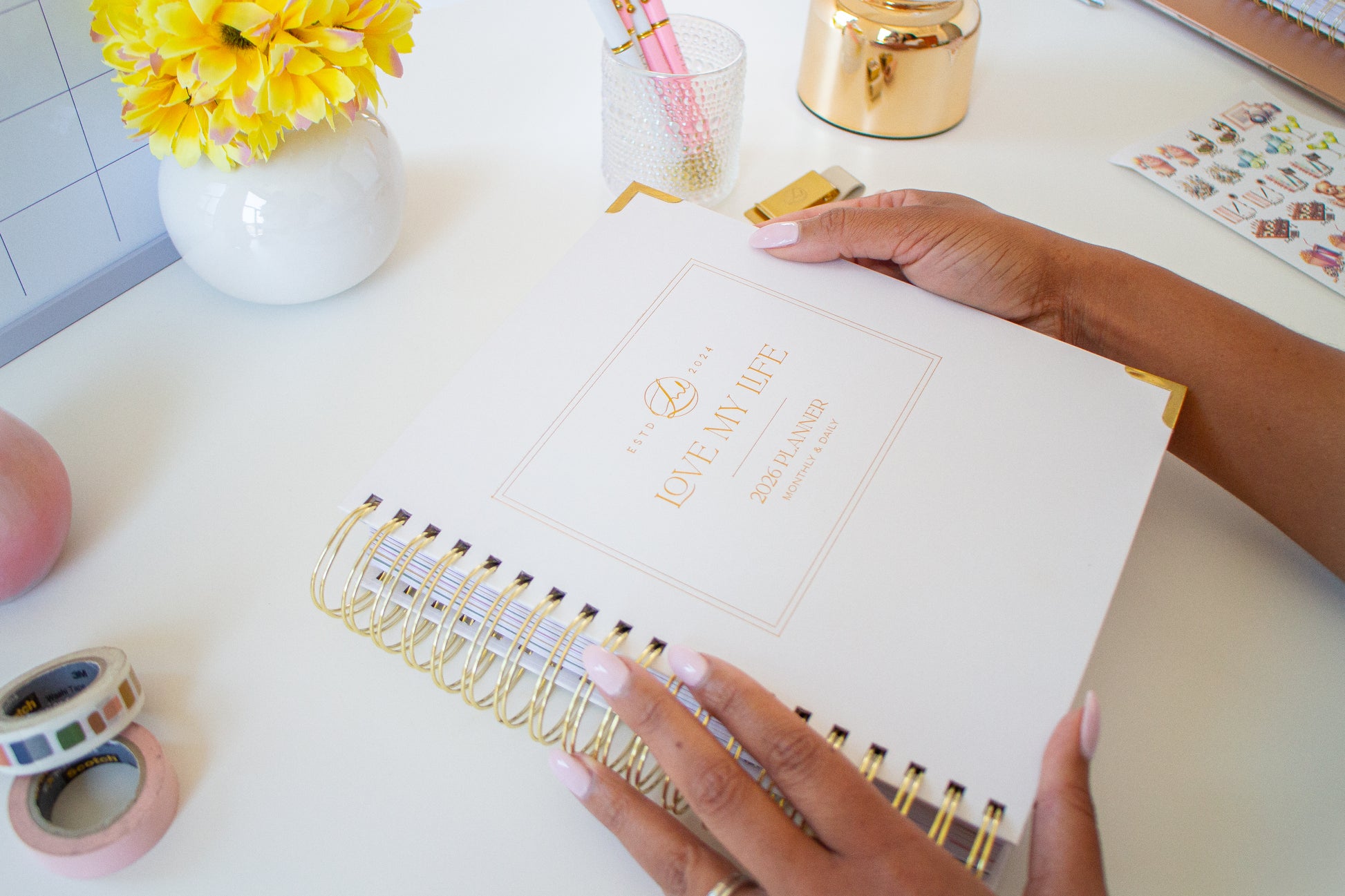 Person holding a planner with decorative items on a desk