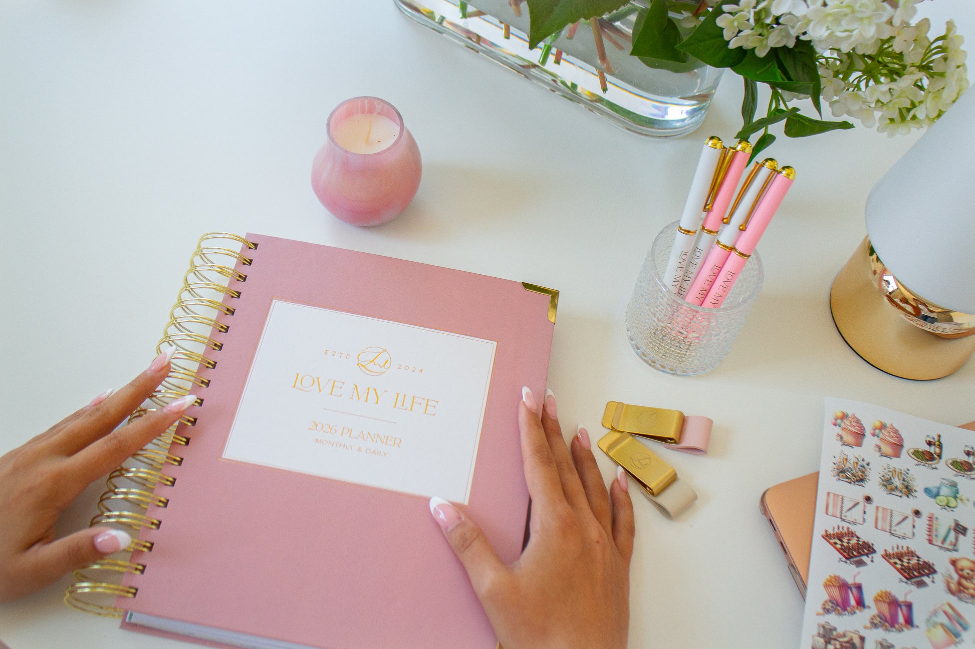 Pink planner with gold spiral binding on a desk with stationery items