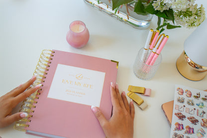 Pink planner with gold spiral binding on a desk with stationery items