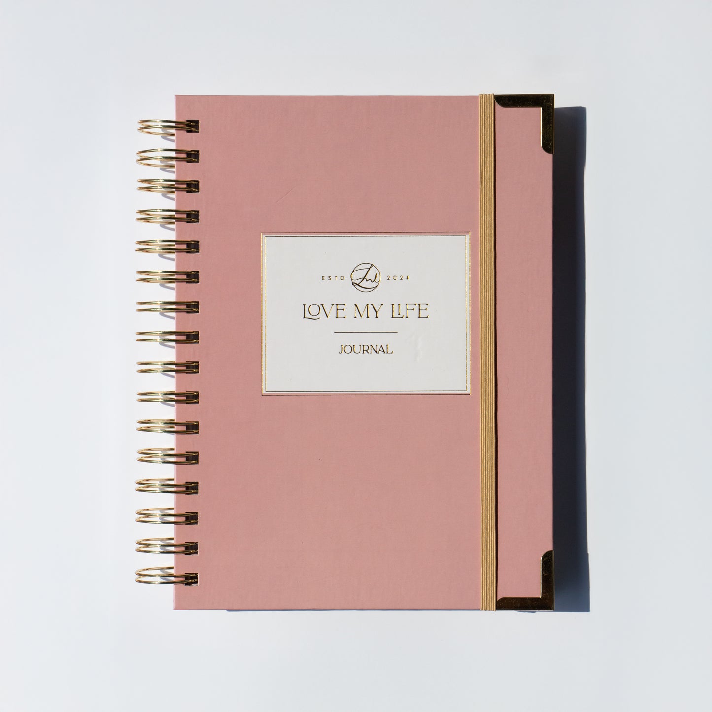 Pink journal with gold spiral binding on a light gray background