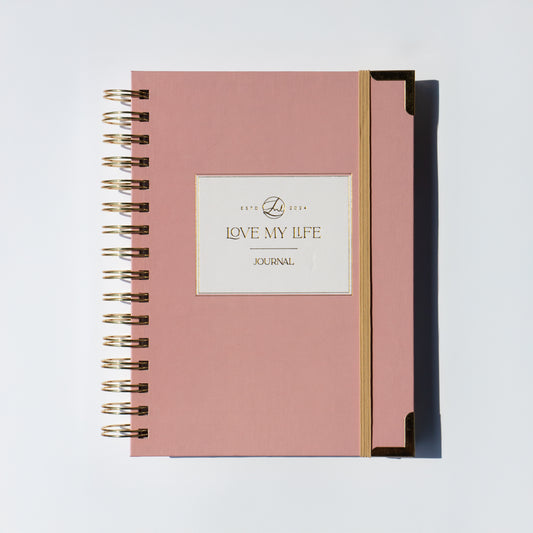 Pink journal with gold spiral binding on a light gray background