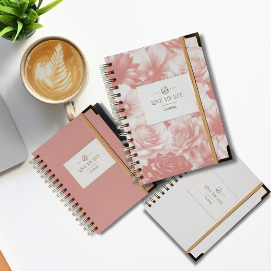 Three notebooks with floral design and 'Love My Life' branding on a white surface with a cup of coffee.
