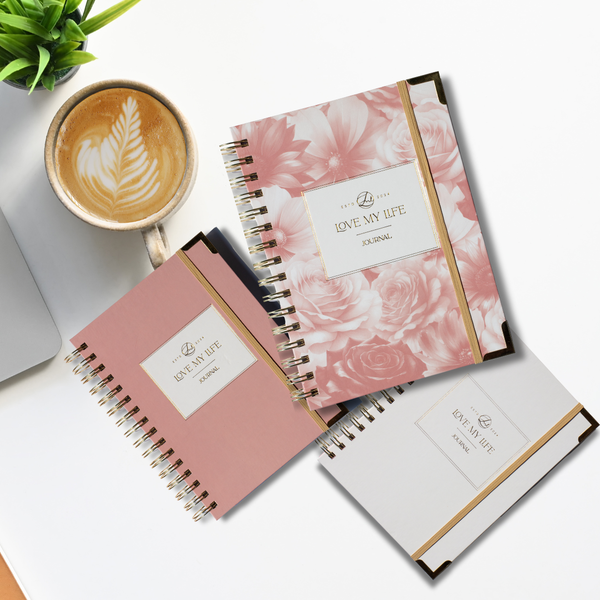 Three notebooks with floral design and 'Love My Life' branding on a white surface with a cup of coffee.